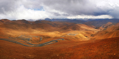 Panoramic view of highway stretching across the brown Himalaya Mountains, against a blue sky covered by white clouds.