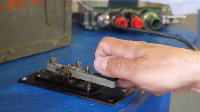 Close up view of man's hand transmitting message by using Morse key, military equipment of 1940-ies.
