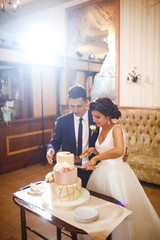 Happy bride and a groom is cutting their stylish wedding cake on wedding banquet. Newlyweds holding knife and cutting together wedding cake decorated with flowers. Sweet cake for couple.