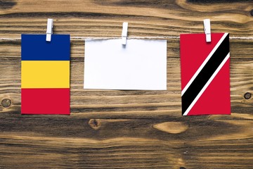 Hanging flags of Romania and Trinidad And Tobago attached to rope with clothes pins with copy space on white note paper on wooden background.Diplomatic relations between countries.