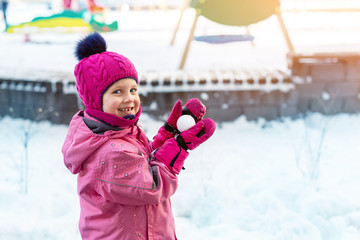 Cute adorable caucasian little girl winter portrait holding snowball in hands ready for snow fight...