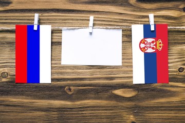 Hanging flags of Russia and Serbia attached to rope with clothes pins with copy space on white note paper on wooden background.Diplomatic relations between countries.