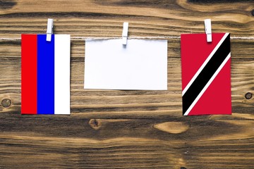 Hanging flags of Russia and Trinidad And Tobago attached to rope with clothes pins with copy space on white note paper on wooden background.Diplomatic relations between countries.