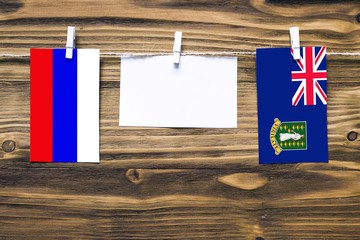 Hanging flags of Russia and British Virgin Islands attached to rope with clothes pins with copy space on white note paper on wooden background.Diplomatic relations between countries.