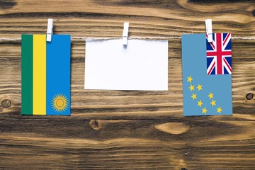 Hanging flags of Rwanda and Tuvalu attached to rope with clothes pins with copy space on white note paper on wooden background.Diplomatic relations between countries.
