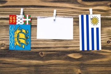 Hanging flags of Saint Pierre And Miquelon and Uruguay attached to rope with clothes pins with copy space on white note paper on wooden background.Diplomatic relations.