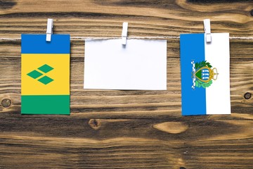 Hanging flags of Saint Vincent And The Grenadines and San Marino attached to rope with clothes pins with copy space on white note paper on wooden background.Diplomatic relations between countries.