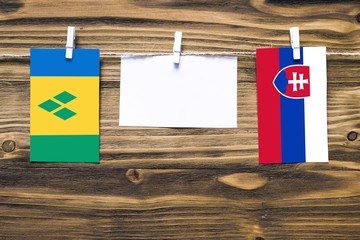 Hanging flags of Saint Vincent And The Grenadines and Slovakia attached to rope with clothes pins with copy space on white note paper on wooden background.Diplomatic relations between countries.