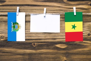 Hanging flags of San Marino and Senegal attached to rope with clothes pins with copy space on white...