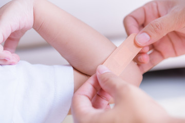 Mother applying adhesive plaster bandage on childen arm wound