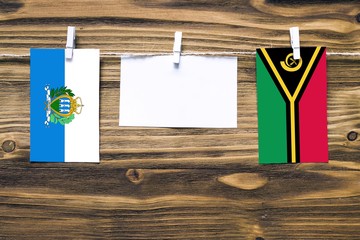 Hanging flags of San Marino and Vanuatu attached to rope with clothes pins with copy space on white...