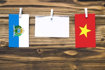Hanging flags of San Marino and Vietnam attached to rope with clothes pins with copy space on white...