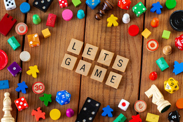 "Lets Game" spelled out in wooden letter tiles. Surrounded by dice, cards, and other game pieces on a wooden background