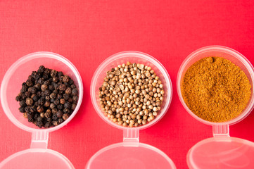 Spices: black pepper, ground red pepper and coriander peas in jars on a red background