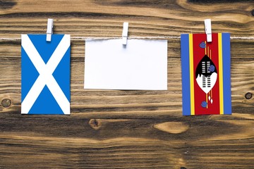 Hanging flags of Scotland and Swaziland attached to rope with clothes pins with copy space on white...
