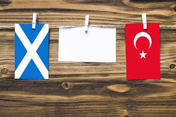 Hanging flags of Scotland and Turkey attached to rope with clothes pins with copy space on white note paper on wooden background.Diplomatic relations between countries.