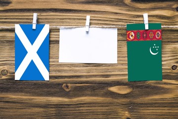 Hanging flags of Scotland and Turkmenistan attached to rope with clothes pins with copy space on...