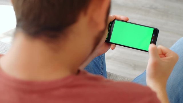 Sports Fan Reaction Concept - Excited sports fan watching his favourite team/player on smartphone with green screen at home, 4k slow motion