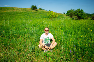 Man in sunglasses sitting on grass with laptop