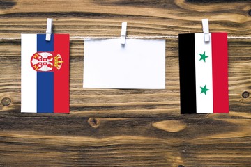 Hanging flags of Serbia and Syria attached to rope with clothes pins with copy space on white note...