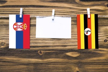 Hanging flags of Serbia and Uganda attached to rope with clothes pins with copy space on white note paper on wooden background.Diplomatic relations between countries.