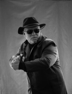 A man in black clothes, a black leather coat, hat. Ganster with a cigar Mauser system pistol. Mafiosi in black glasses on a dark background. Severe, strong, stylish, impressive, dangerous, unfriendly,