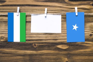 Hanging flags of Sierra Leone and Somalia attached to rope with clothes pins with copy space on white note paper on wooden background.Diplomatic relations between countries.