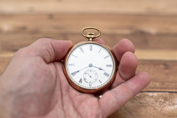 Gold pocket watch held by a man's hand and with a ring.