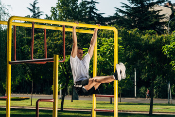 Strong young muscular man doing pull-up exercise at the outdoors gym