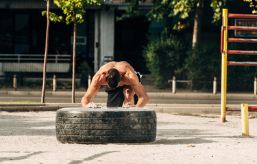 Active shirtless man in sportswear flipping tyre in crossfit center