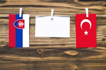 Hanging flags of Slovakia and Turkey attached to rope with clothes pins with copy space on white note paper on wooden background.Diplomatic relations between countries.