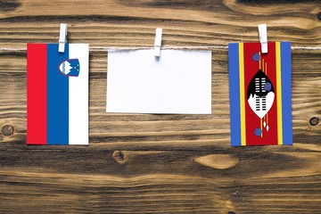 Hanging flags of Slovenia and Swaziland attached to rope with clothes pins with copy space on white note paper on wooden background.Diplomatic relations between countries.
