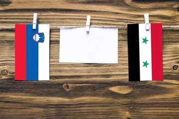 Hanging flags of Slovenia and Syria attached to rope with clothes pins with copy space on white...