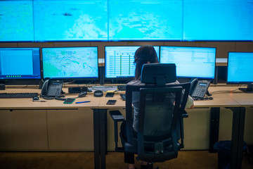 Female security guard sitting back and monitoring modern CCTV cameras in a surveillance room.