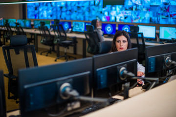 Fototapeta na wymiar Female security guard sitting and monitoring modern CCTV cameras in surveillance room.