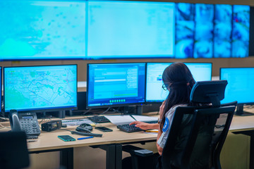 Female security guard sitting back and monitoring modern CCTV cameras in a  surveillance room.