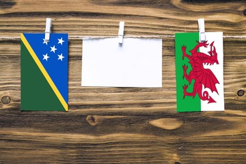 Hanging flags of Solomon Islands and Wales attached to rope with clothes pins with copy space on...