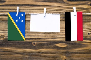 Hanging flags of Solomon Islands and Yemen attached to rope with clothes pins with copy space on...