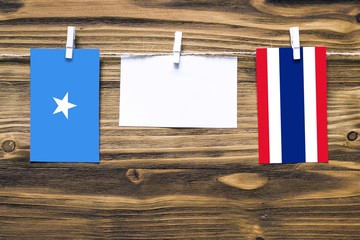 Hanging flags of Somalia and Thailand attached to rope with clothes pins with copy space on white note paper on wooden background.Diplomatic relations between countries.