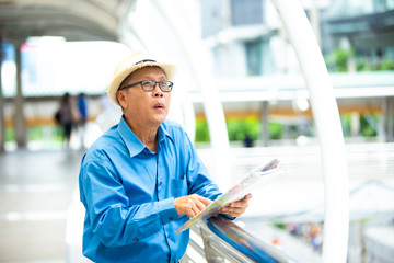 Old senior man of backpackers holding in hands travel map and walking by the city. Happy Travel and tourism concept.