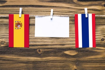 Hanging flags of Spain and Thailand attached to rope with clothes pins with copy space on white note paper on wooden background.Diplomatic relations between countries.