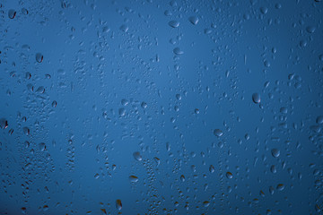 Wassertropfen bei Regenwetter am Fenster mit blauen Hintergrund