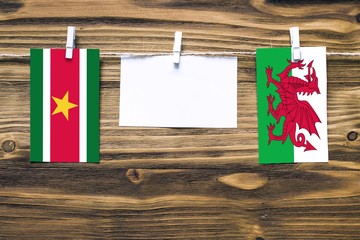 Hanging flags of Suriname and Wales attached to rope with clothes pins with copy space on white note paper on wooden background.Diplomatic relations between countries.