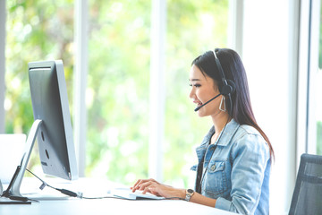 Attractive business woman Asian in suits and headsets are smiling while working with computer at office. Customer service assistant working in office