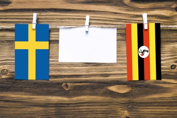 Hanging flags of Sweden and Uganda attached to rope with clothes pins with copy space on white note paper on wooden background.Diplomatic relations between countries.