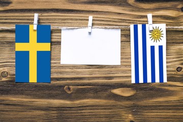 Hanging flags of Sweden and Uruguay attached to rope with clothes pins with copy space on white note paper on wooden background.Diplomatic relations between countries.