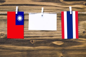 Hanging flags of Taiwan and Thailand attached to rope with clothes pins with copy space on white note paper on wooden background.Diplomatic relations between countries.