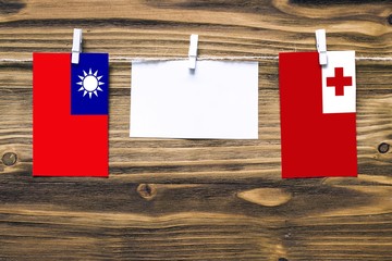 Hanging flags of Taiwan and Tonga attached to rope with clothes pins with copy space on white note paper on wooden background.Diplomatic relations between countries.