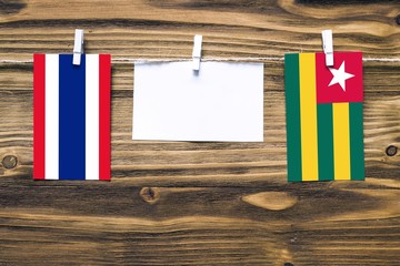 Hanging flags of Thailand and Togo attached to rope with clothes pins with copy space on white note paper on wooden background.Diplomatic relations between countries.