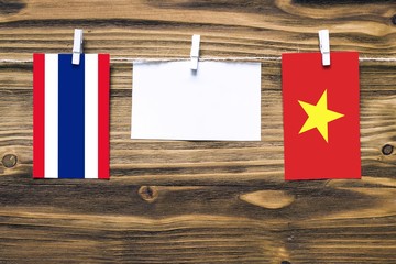 Hanging flags of Thailand and Vietnam attached to rope with clothes pins with copy space on white note paper on wooden background.Diplomatic relations between countries.